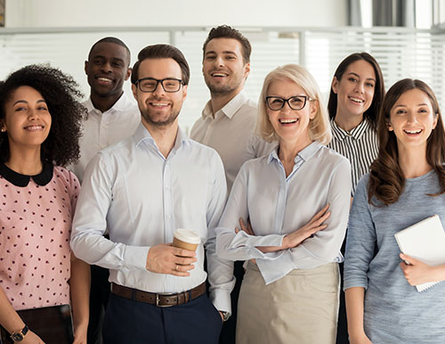 Smiling multiethnic employees standing looking at camera making team picture in office together, happy diverse work group or department laugh posing for photo at workplace, show unity and cooperation